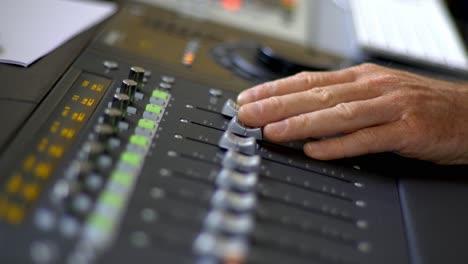 Hands-moving-faders-on-an-audio-mixing-table-in-a-recording-studio