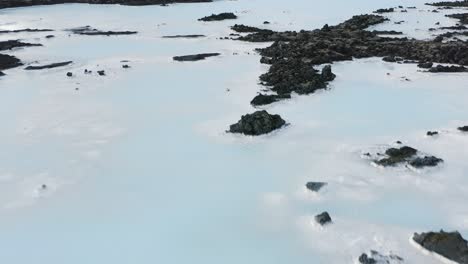 Natural-milky-pools-surrounded-by-black-volcanic-rock-in-Iceland,-aerial