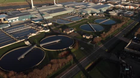 Backwards-aerial-view-of-a-water-treatment-facility-in-The-Netherlands-showing-the-various-circular-and-rectangular-forms-revealing-the-rotating-blades-of-a-wind-turbine-in-the-foreground