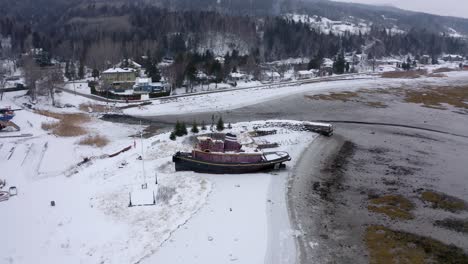 Drone-flying-around-a-beautiful-old-boat-under-the-snow-in-a-shipyard-in-Charlevoix,-Quebec