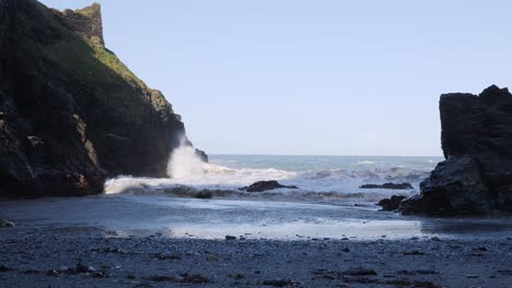 Half-speed-shot-of-waves-crashing-onto-a-beach-over-large-rocks