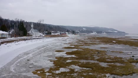 Drohne-Fliegt-Im-Winter-über-Den-Zugefrorenen-Fluss-Am-Rande-Eines-Kleinen-Dorfes