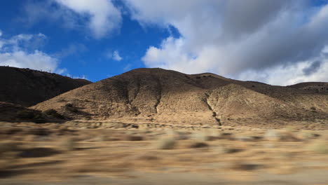 Driving-along-the-foothills-near-Tehachapi,-California-and-watching-a-dynamic-cloudscape-over-the-grassy-landscape---passenger-window-point-of-view-hyper-lapse