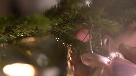 Close-up-of-hand-decorating-Christmas-Pine-Tree-with-Xmas-ornament-bauble-ball