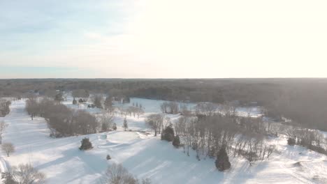 A-crawling-slow-drone-shot-of-a-snow-covered-golf-course-showing-the-indents-of-course-features,-trees,-and-the-peaceful-landscape