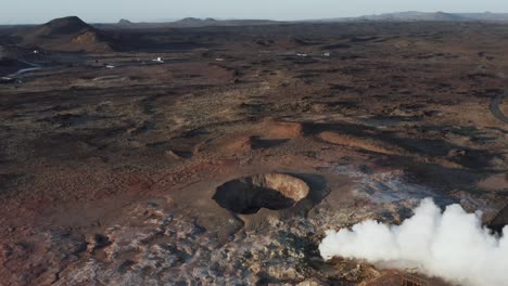 Active-volcanic-geyser-with-white-steam-in-rugged-Iceland-landscape,-aerial