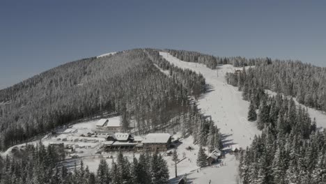 Kope-resort-and-hotel-n-the-Pohorje-mountains-Slovenia-with-skiers-descending-Ribnica-One-track,-Aerial-pan-right-shot