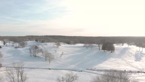 A-gentle-descent-to-show-the-horizon,-a-lovely-and-peaceful-snow-covered-golf-course,-all-via-drone
