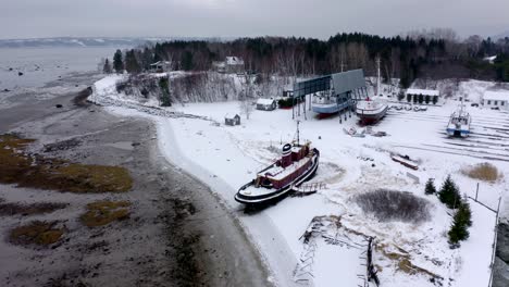 Drone-flying-around-an-old-ship-in-wintertime-in-Charlevoix,-Quebec