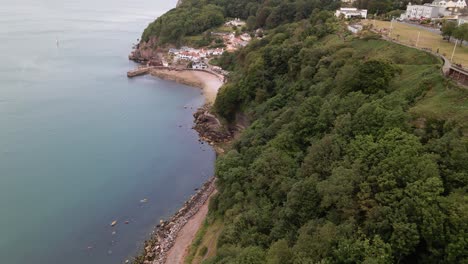 Aerial-flyover-beautiful-landscape-with-green-cliff-hills-and-rocky-beach-and-blue-shore-in-Torquay-City,Devon