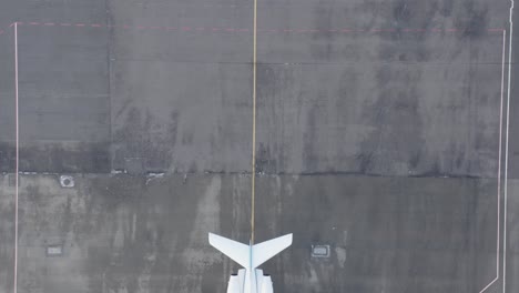 Top-down-aerial-revealing-white-private-jet-parked-on-grey-tarmac-at-airbase