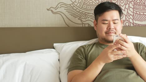 Ein-Junger-Mann-Nutzt-Sein-Handy-Zum-Online-einkaufen-Und-Chattet-Auf-Dem-Bett-Im-Schlafzimmer