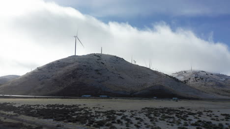 A-highway-overshadowed-by-tall-wind-turbines-on-a-hillside-in-winter-on-a-cloudy-day
