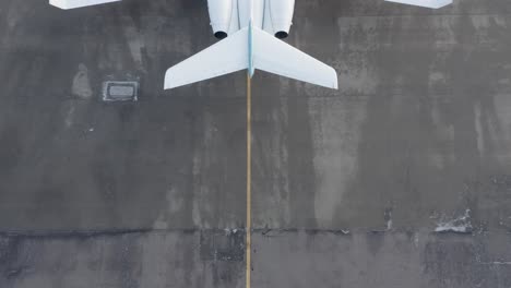Behind-large-private-airplane-parked-on-concrete-airport,-reveal-shot