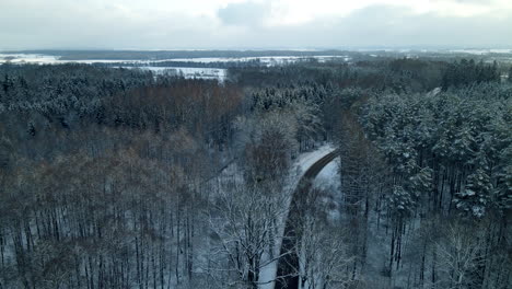 Drone-flying-over-snow-covered-forest-with-a-curved-road,-aerial-view