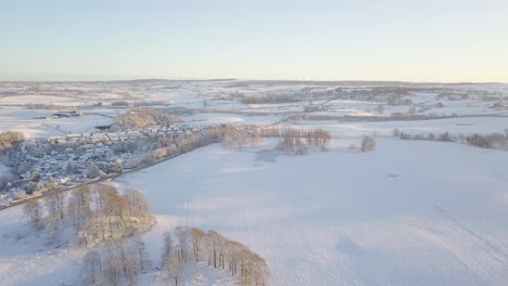 Winterlandschaft-Mit-Einem-Dorf-Mit-Großen-Häusern-Und-Mit-Weißem-Schnee-Bedeckten-Feldern-Und-Einer-Geräumten-Asphaltstraße-An-Einem-Hellen,-Kalten-Tag-In-Schottland-Während-Der-Goldenen-Stunde