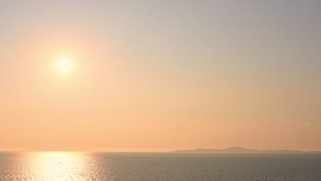 Evocative-shot-of-bright-sun-reflecting-over-sea-with-mountain-in-background