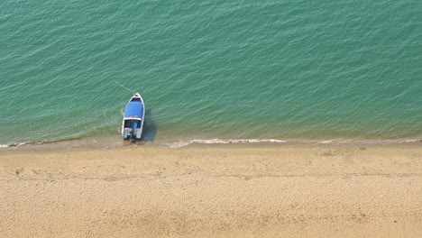 A-high-angle,-a-single-boat-anchored-at-a-golden-sandy-beach