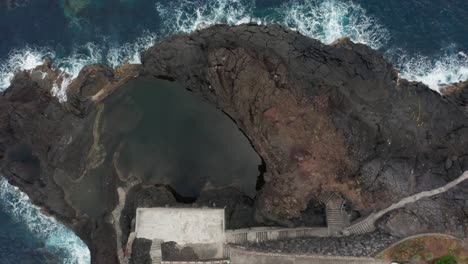 Top-down-aerial-of-natural-swimming-pools-between-rocky-volcanic-shore,-Madeira