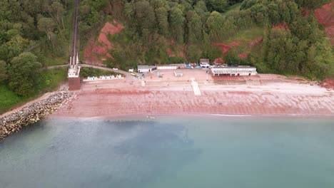 Aerial-dolly-flight-showing-popular-Oddicombe-Beach-with-blue-ocean-water,-red-sand-and-breccia-cliffs
