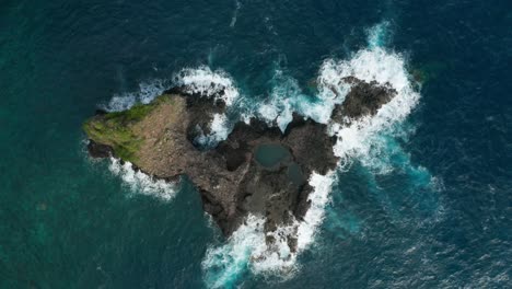 Volcanic-basalt-island-surrounded-by-rough-blue-water-of-Atlantic-Ocean,-aerial