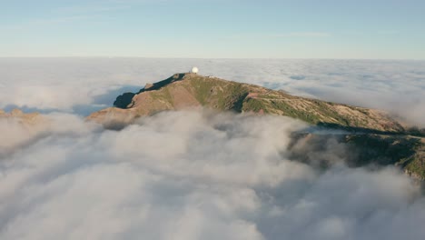 Clouds-surrounding-mountain-with-weather-station-on-top-in-Madeira,-aerial