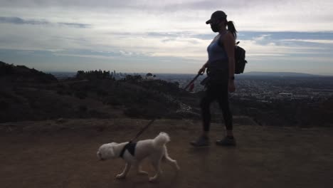 Female-walking-dog-in-Griffith-Park,-top-of-mountain-over-Griffith-Observatory