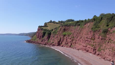 Aerial-forward-flight-along-Ness-Cove-Beach-and-red-clay-cliff-in-Shaldon,-South-Devon,-England