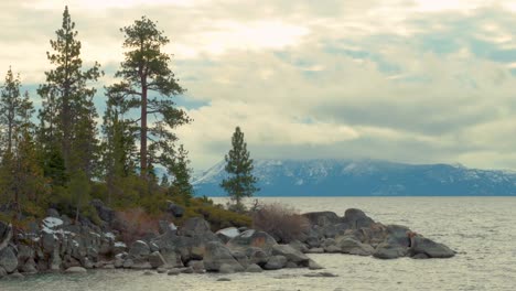 Tall-pine-trees-growing-on-top-of-large-rock-formations-in-Sand-Harbor,-South-Lake-Tahoe,-Nevada-surrounded-snow-capped-Sierra-Mountains