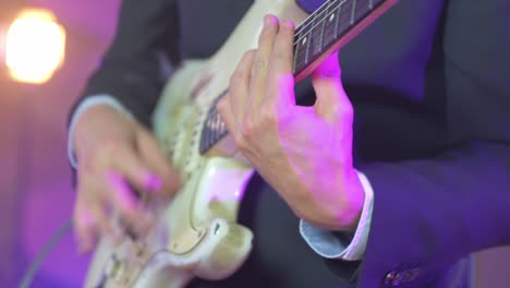 Close-up-of-a-professional-musician-playing-chords-on-an-electric-stratocaster-guitar-during-a-live-session-on-stage-with-warm-studio-lights-in-the-blurred-background