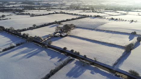 Cold-snowy-winter-British-patchwork-farmland-countryside-rural-scene-aerial-slow-orbiting-left-at-sunrise