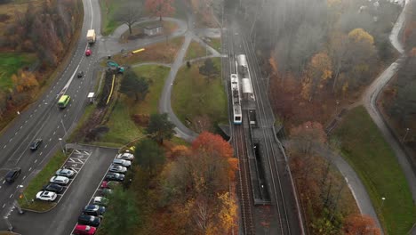 Aerial-View-of-Passing-Train-near-a-Busy-Road-on-a-Foggy-Day,-Pullback
