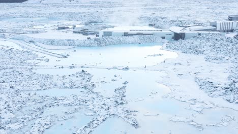 People-walking-in-snow-at-blue-lagoon-pools-outside-of-spa,-aerial