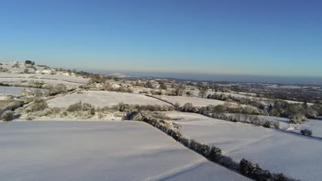 Cold-snowy-winter-British-patchwork-farmland-countryside-rural-scene-aerial-rising-right-pan-at-sunrise