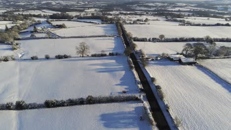 Cold-snowy-winter-British-patchwork-farmland-countryside-rural-scene-aerial-left-orbit-at-sunrise