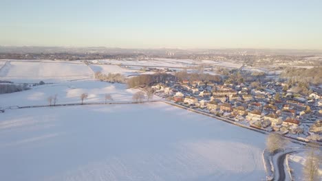 Winter-landscape-near-a-village-with-big-houses-and-fields-covered-with-white-snow-till-the-horizon-on-a-bright-cold-day-in-Scotland-during-golden-hour