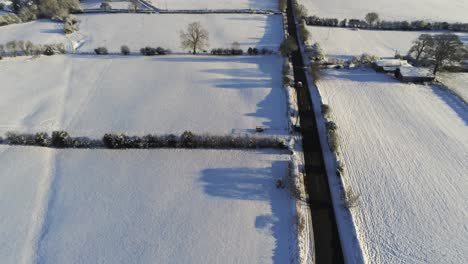 Tracking-fast-vehicle-on-long-road-in-cold-snowy-winter-British-patchwork-farmland-countryside-at-sunrise