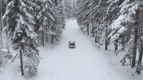Aerial-shot-of-a-sport-car-riding-on-a-snowy-road-between-snow-covered-trees-in-forest-on-a-cold,-winter-day---drone-shot,-low-angle,-follow