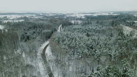 Aerial-view-showing-asphalt-road-surrounded-by-beautiful-snow-covered-tree-landscape-in-winter