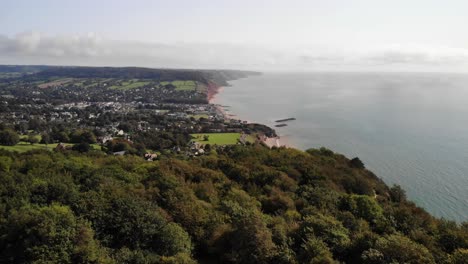 Aerial-footage-flying-over-trees-looking-towards-Sidmouth-and-Lyme-Bay,-Devon-UK