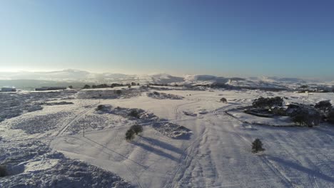 Snow-covered-rural-winter-countryside-track-footprint-shadows-terrain-aerial-view-rising-pan-right-tilting-down