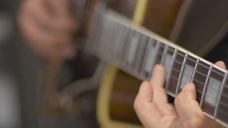 Close-up-of-a-professional-musician-playing-a-solo-on-a-hollow-body-electric-guitar-with-a-guitar-pick-during-a-recording-session-in-a-studio-with-a-blurred-background