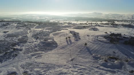 Snow-covered-rural-winter-countryside-track-footprint-shadows-terrain-aerial-view-pan-right-across-highlands