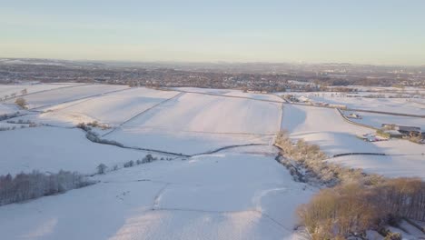 Rural-winter-landscape-with-a-house-and-fields-covered-with-white-snow-till-the-horizon-on-a-bright-cold-day-in-Scotland-during-golden-hour