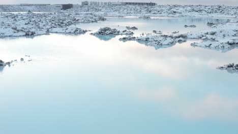 Stunning-blue-lagoon-pools-reflect-sky-in-snowy-rugged-landscape-of-iceland