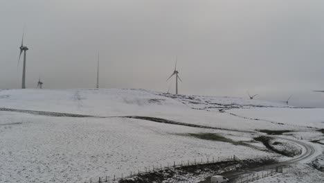 Winter-mountain-countryside-wind-turbines-on-rural-highlands-aerial-view-cold-snowy-valley-hillside-pan-right-shot