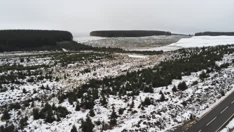 Long-road-aerial-into-distance-across-highland-snowy-countryside-moors-establishing-right-shot