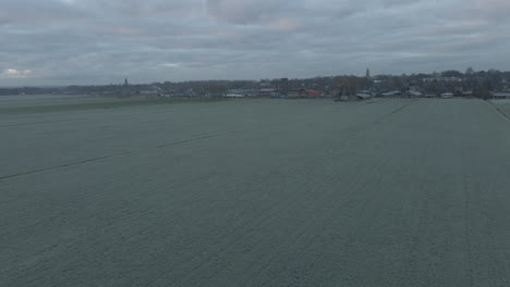 Aerial-of-frozen-meadows-with-a-town's-skyline-in-the-background