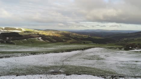 Snowy-rural-winter-valley-countryside-aerial-agricultural-farmland-moorland-left-pan-descending