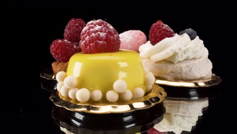 macro-view-turning-colorful-pastries-on-black-reflective-glass-background,-luxury-patisserie-4k,-pavlova,-macaron,-raspberry-tart,-mango-small-cake